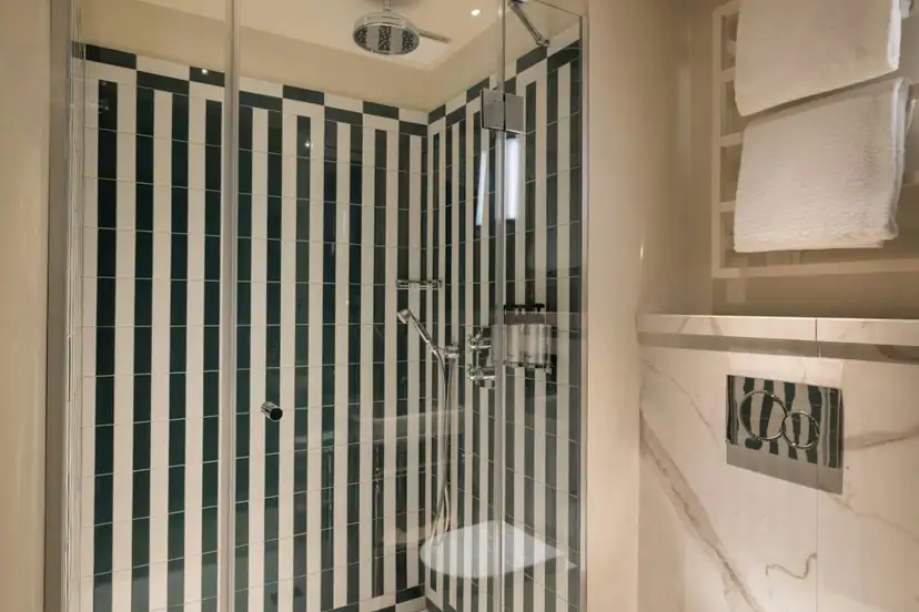 Glass-enclosed walk-in shower with a rain showerhead, handheld sprayer, and bold striped tile.